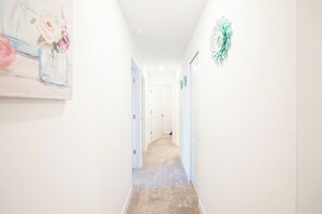 A hallway with a carpeted floor, white walls, and a door at the end. - Newly Remodeled House Near Disney (Davenport)