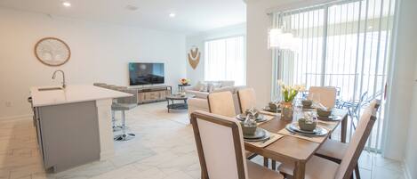 A modern kitchen with a dining area, a flat-screen TV, and a large window.
