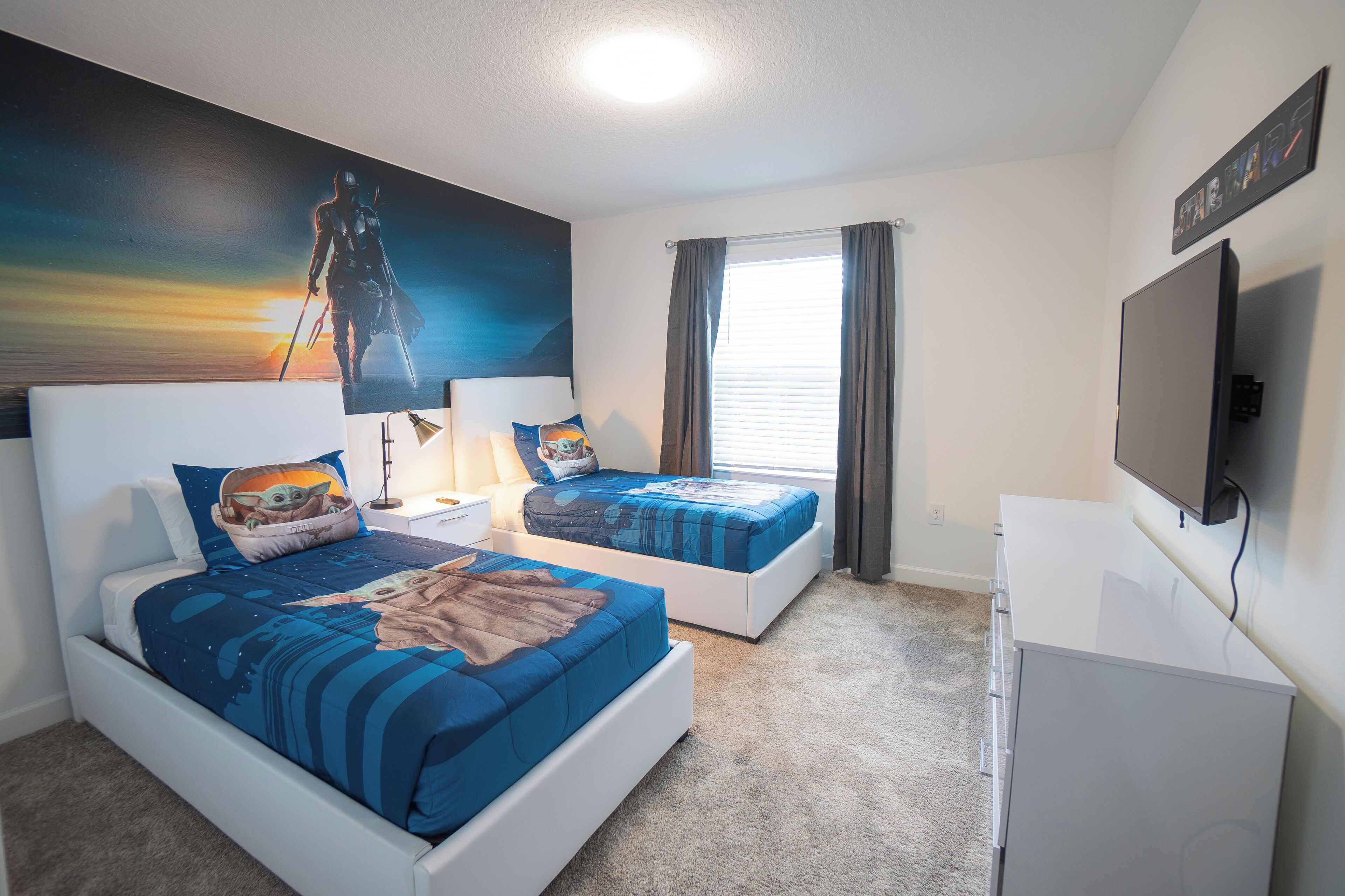 A bedroom with two beds, a painting on the wall, a window with curtains, and a TV on the wall.