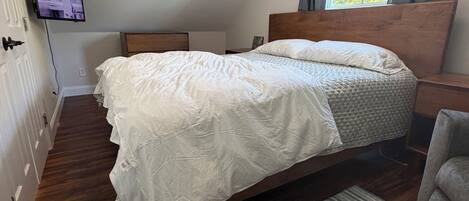 Un dormitorio con cama, televisión, ventana con cortinas y suelo de madera.