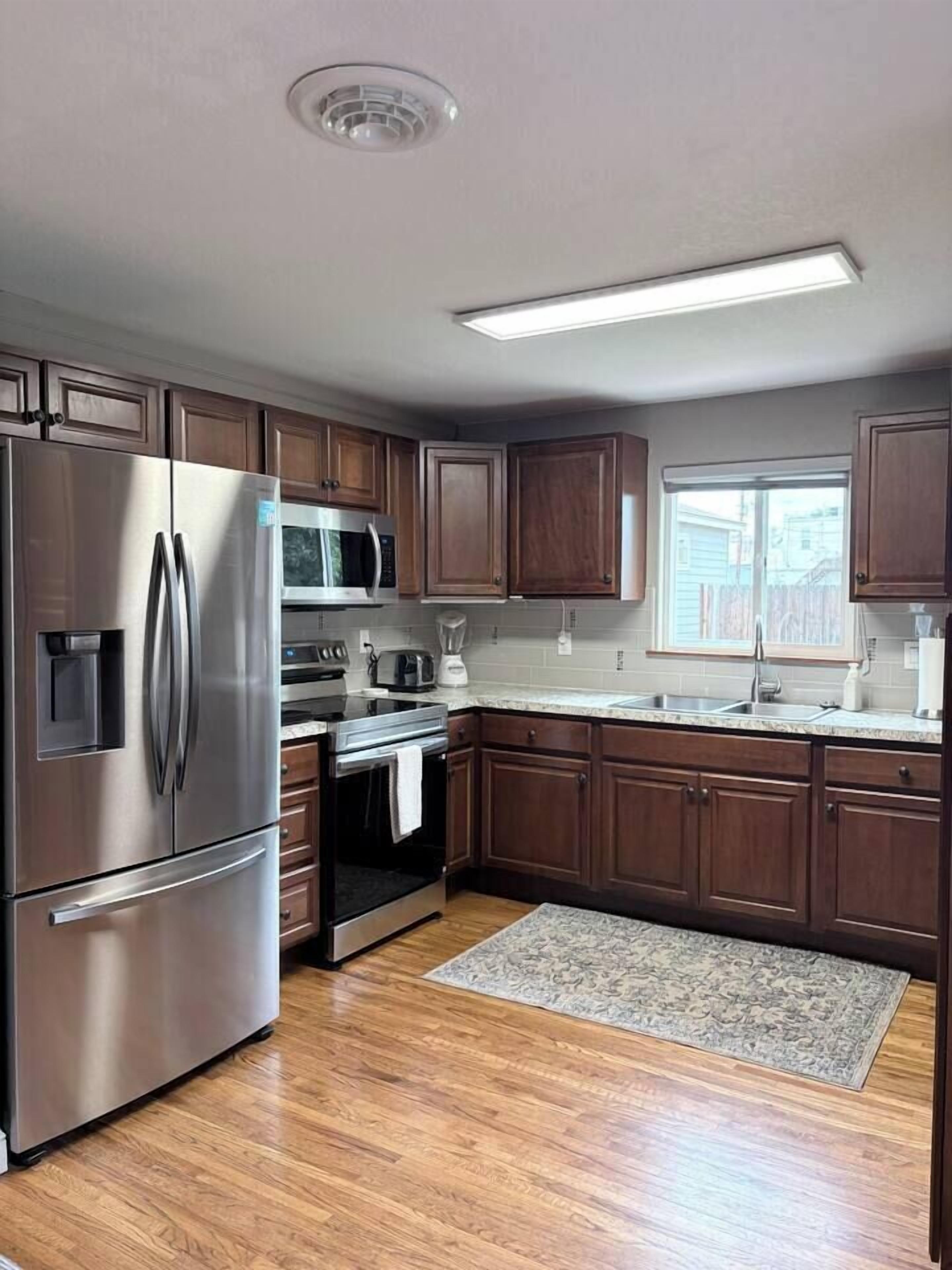 A modern kitchen with stainless steel appliances, wooden cabinets, and a large window.