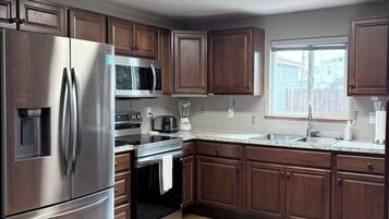 A modern kitchen with stainless steel appliances, wooden cabinets, and a large window.