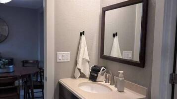 A bathroom with a sink, mirror, and vanity. There is a towel hanging on the wall and a bag on the counter.