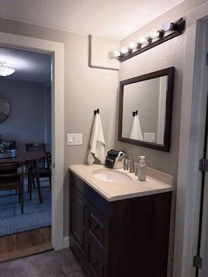 A bathroom with a sink, mirror, and vanity. There is a towel hanging on the wall and a bag on the counter. - The Windsor Exchange Retreat (Windsor)