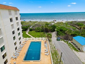 A swimming pool with lounge chairs, a beach view, and a pathway leading to the beach. - New Oceanfront 2-bedroom 2 bath condo in pristine Cocoa Beach condo with Pool (Cocoa Beach)