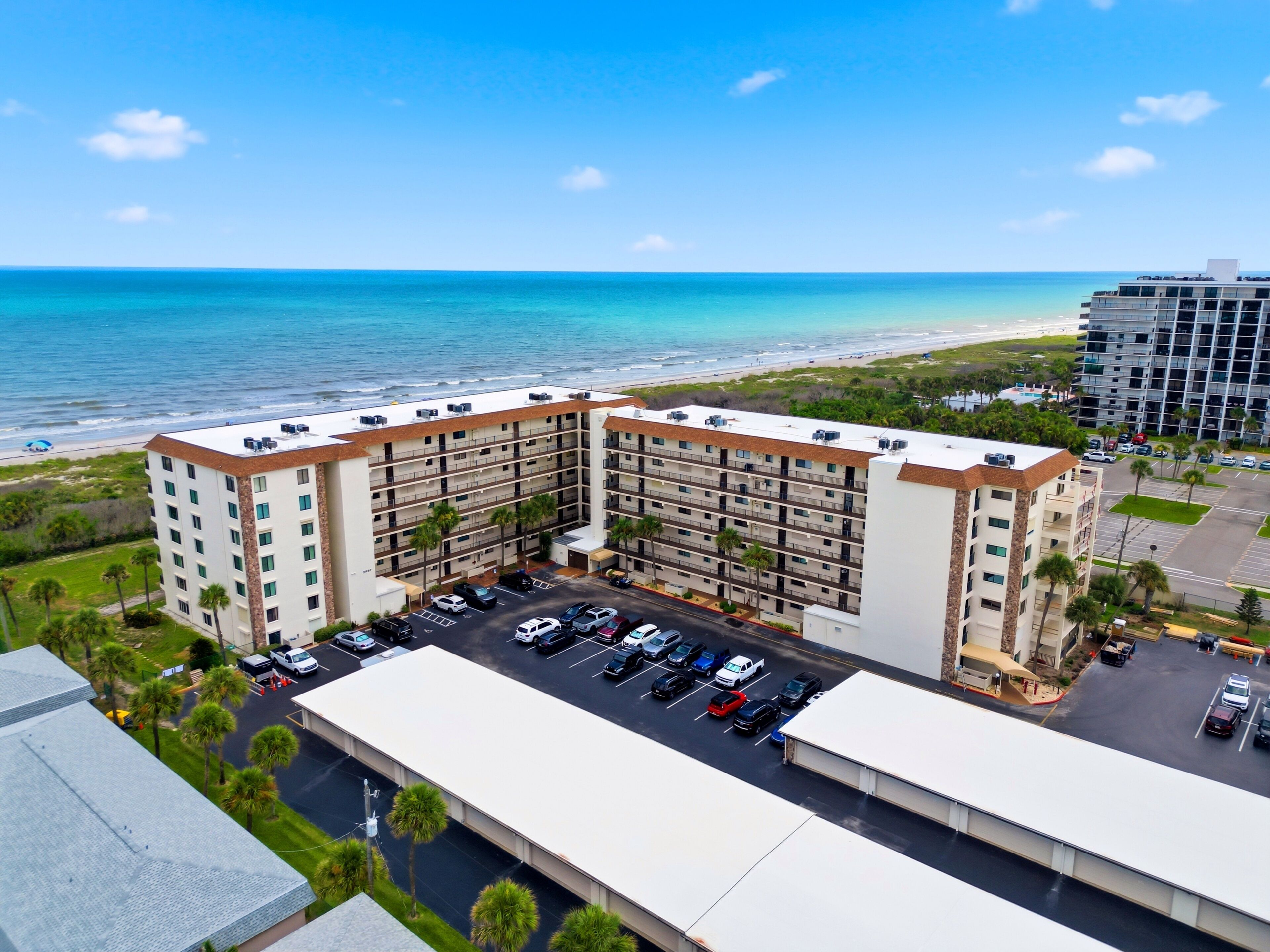 A multi-story hotel with a parking lot and a view of the beach.