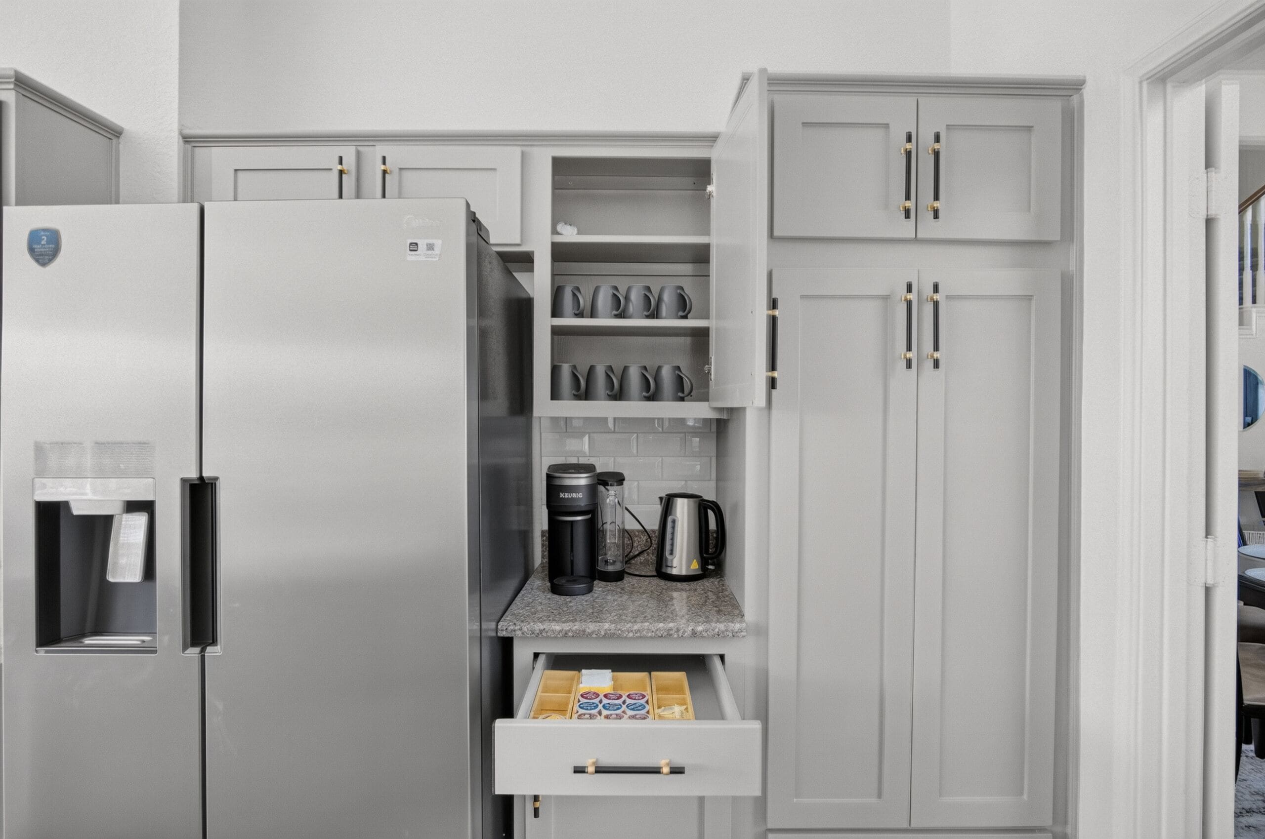 A modern kitchen with a stainless steel refrigerator, a coffee maker, and a kettle on the countertop.