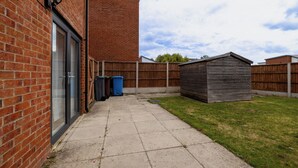 A backyard with a brick wall, a wooden shed, and a concrete patio. - E-Solace-  Etihad-Coop LIVE-Free Parking-Pool Table (Manchester)