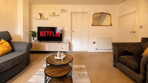 A living room with a flat-screen TV displaying 'NETFLIX,' a sofa, a coffee table, and a staircase in the background. - E-Solace-  Etihad-Coop LIVE-Free Parking-Pool Table (Manchester)