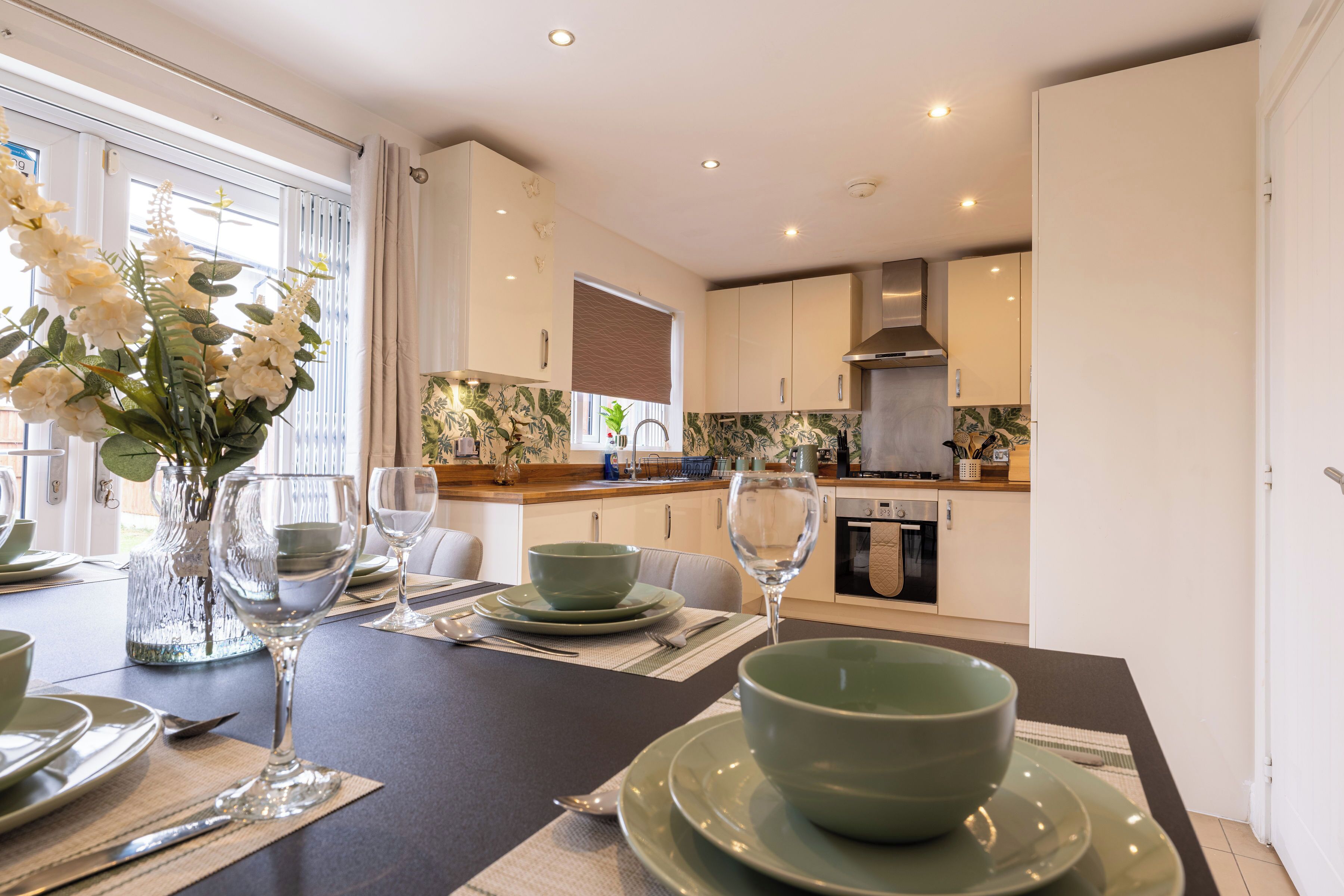 A modern kitchen with white cabinets, a stainless steel range hood, and a dining area with a table set for two.