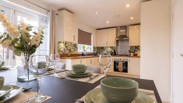 A modern kitchen with white cabinets, a stainless steel range hood, and a dining area with a table set for two.