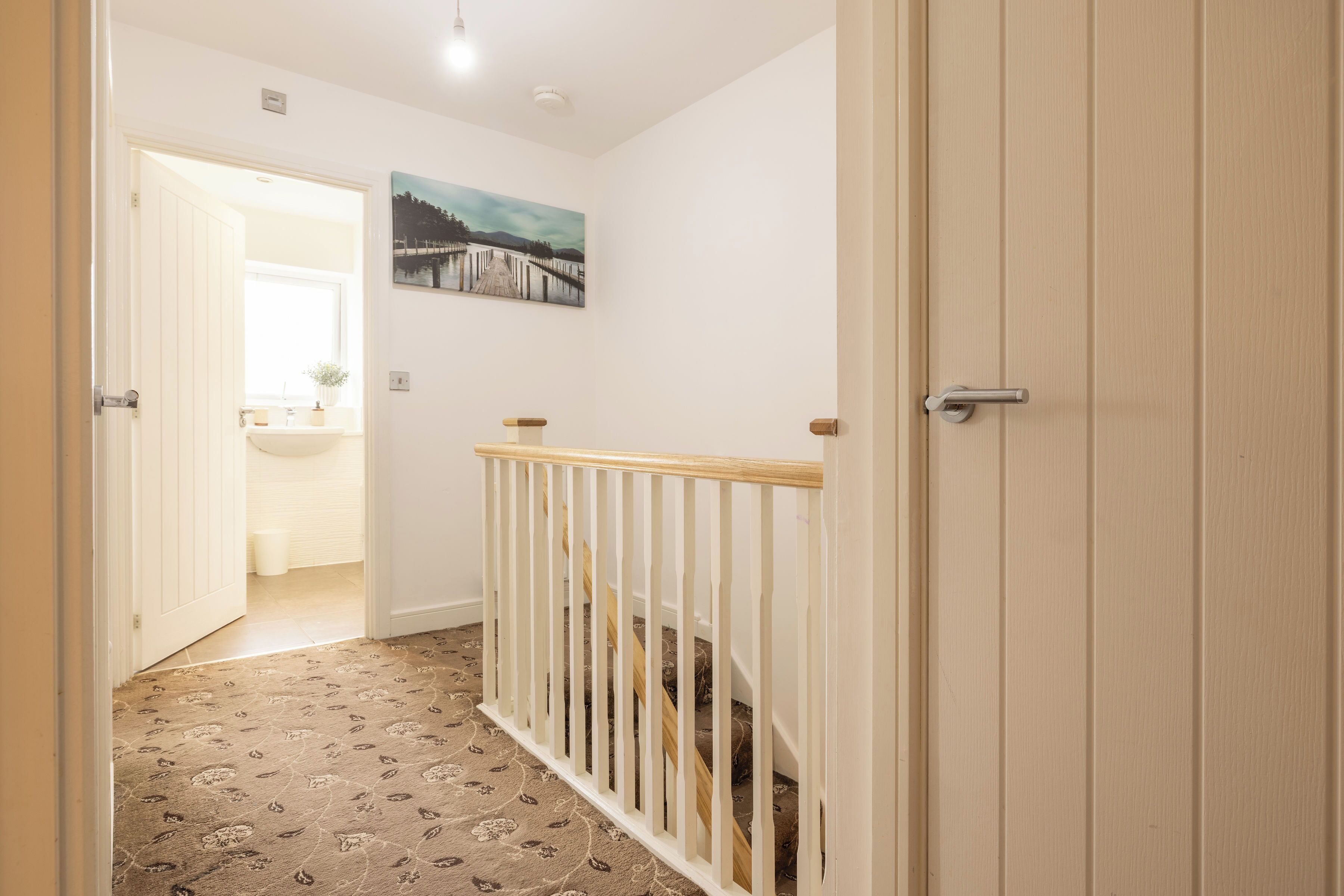 A hallway with a wooden railing, a painting on the wall, and a door leading to a bathroom.