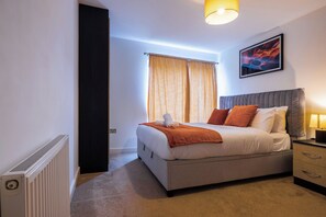 A bedroom with a bed, bedside table, lamp, and a painting on the wall.