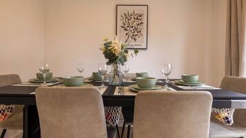 A dining table set with green bowls, plates, and wine glasses, with a framed botanical print on the wall.