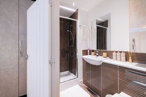 A modern bathroom with a walk-in shower, a vanity with a mirror, and toiletries.