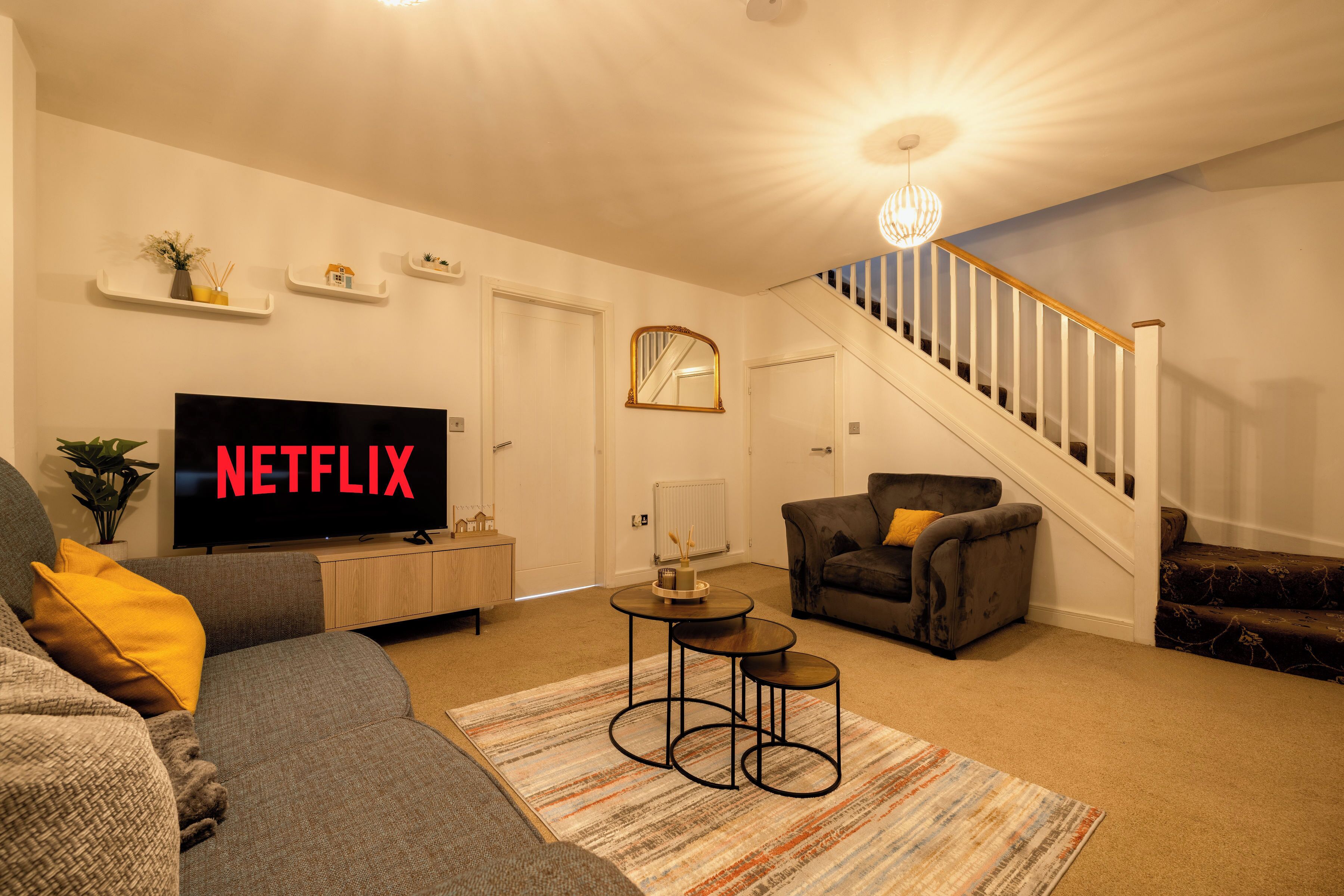 A living room with a flat-screen TV, a sofa, a chair, a coffee table, and a staircase.