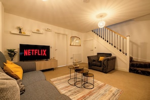 A living room with a flat-screen TV, a sofa, a chair, a coffee table, and a staircase.