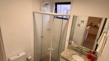A bathroom with a glass-enclosed shower, a toilet, a sink with a mirror, and a window.
