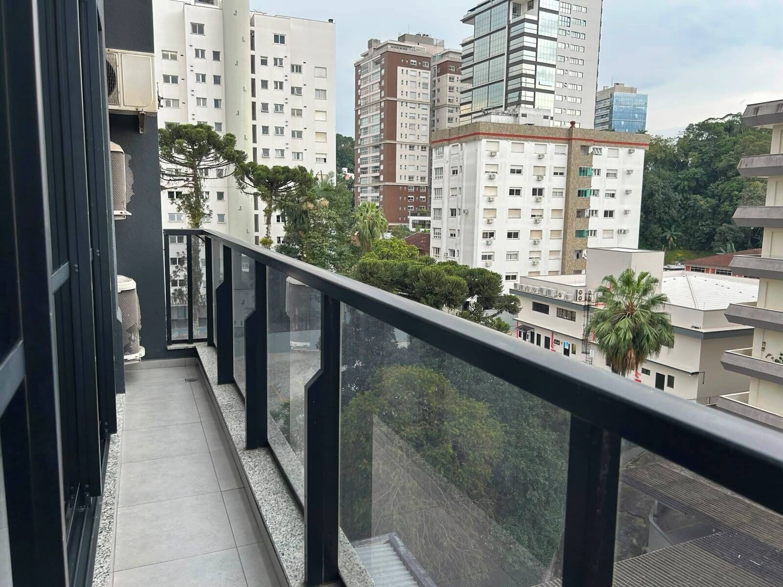 Un balcon doté d’une balustrade en verre, offrant une vue sur un paysage urbain composé de différents bâtiments et d’espaces verts.