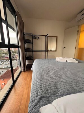 Habitación de hotel con cama, ventana, estante con objetos colgantes y puerta.