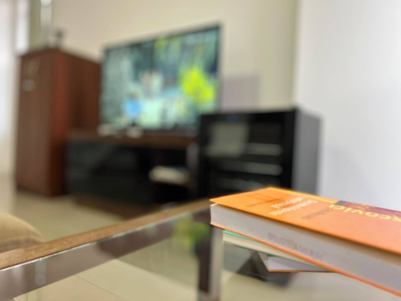 Una habitación con una mesa de vidrio, un libro, un televisor y un armario.