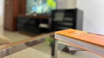 Una habitación con una mesa de vidrio, un libro, un televisor y un armario.