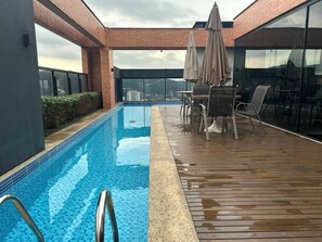 A rooftop swimming pool with a wooden deck, lounge chairs, and umbrellas.