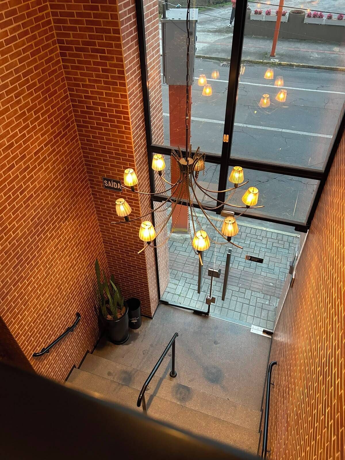 Una escalera con un muro de ladrillo, una araña con múltiples luces y una planta en maceta.