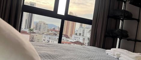 Una habitación de hotel con cama, ventana con cortinas y vista a edificios.