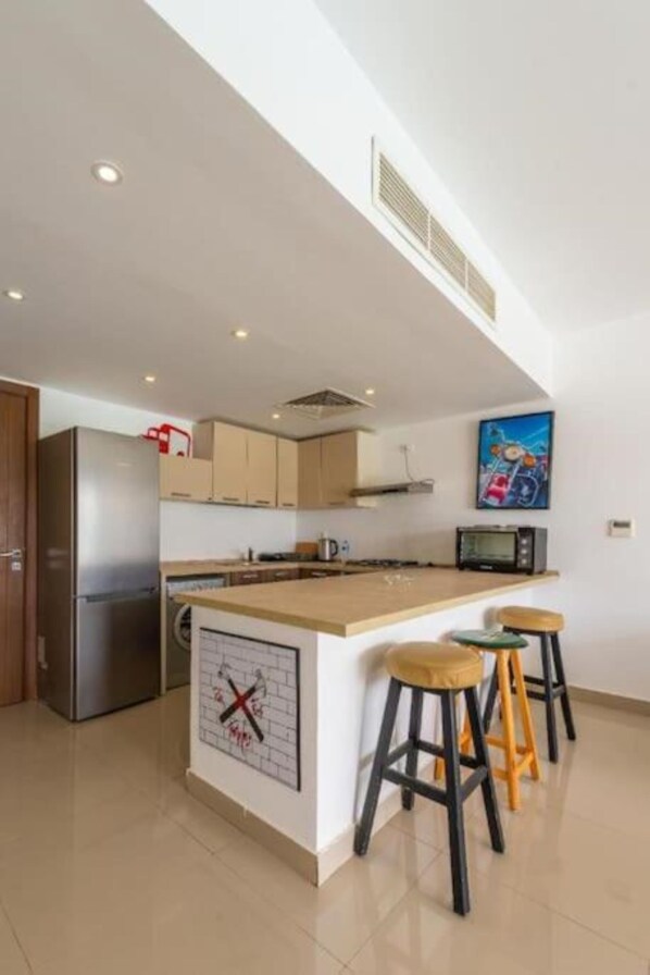 A modern kitchen with a central island, bar stools, a refrigerator, and a microwave.