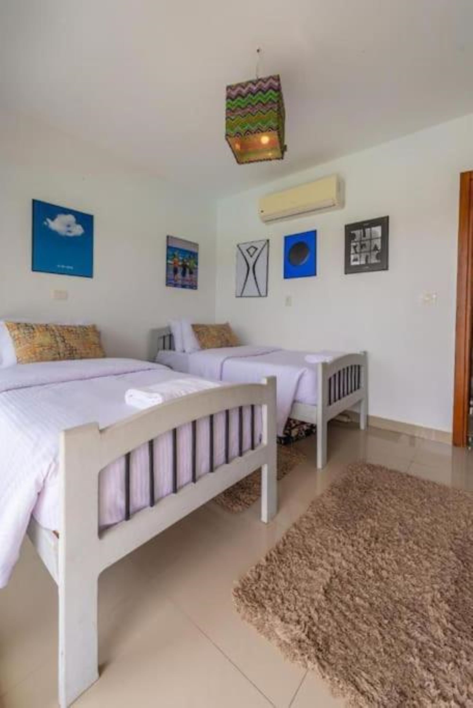 A bedroom with two beds, a rug, and wall art.