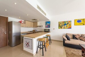 A modern kitchen with a central island, bar stools, a refrigerator, and a microwave.