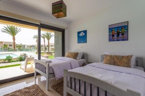A hotel room with two beds, a large window, a view of a pool, and a painting on the wall.