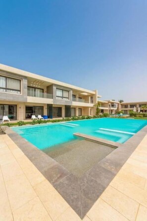 A modern hotel with a swimming pool, multiple balconies, and a clear blue sky.