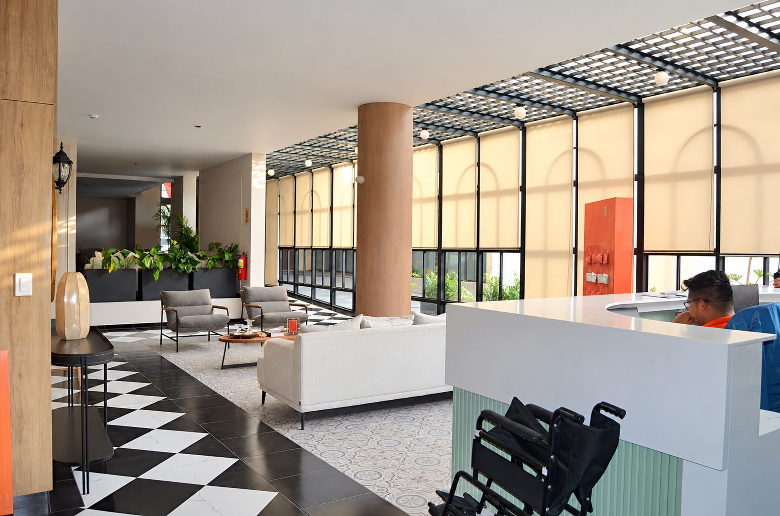 Eine moderne Lobby mit Schachbrettmuster-Boden, Sitzbereichen, einem Empfangstresen und großen Fenstern für natürliches Licht.