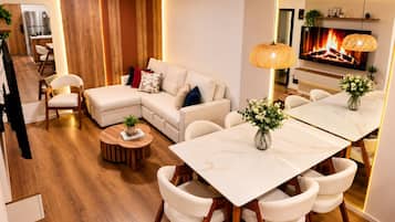 A modern living room with a sectional sofa, a dining table with chairs, a TV, and a fireplace.