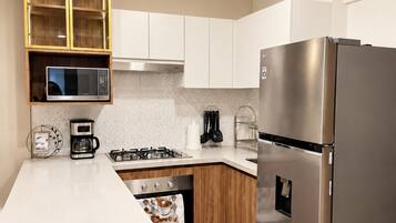 A modern kitchen with a stainless steel refrigerator, a built-in oven, a coffee maker, and wooden cabinetry.