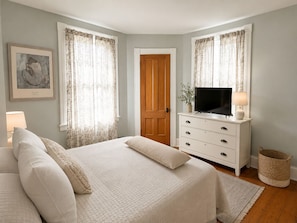 A bedroom with a bed, a dresser, a television, and a window with curtains. - The Yellow House - Walk to Downtown Mystic (Stonington)