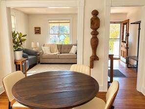 A dining area with a round table and chairs, a sofa, a lamp, and a potted plant. - The Yellow House - Walk to Downtown Mystic (Stonington)