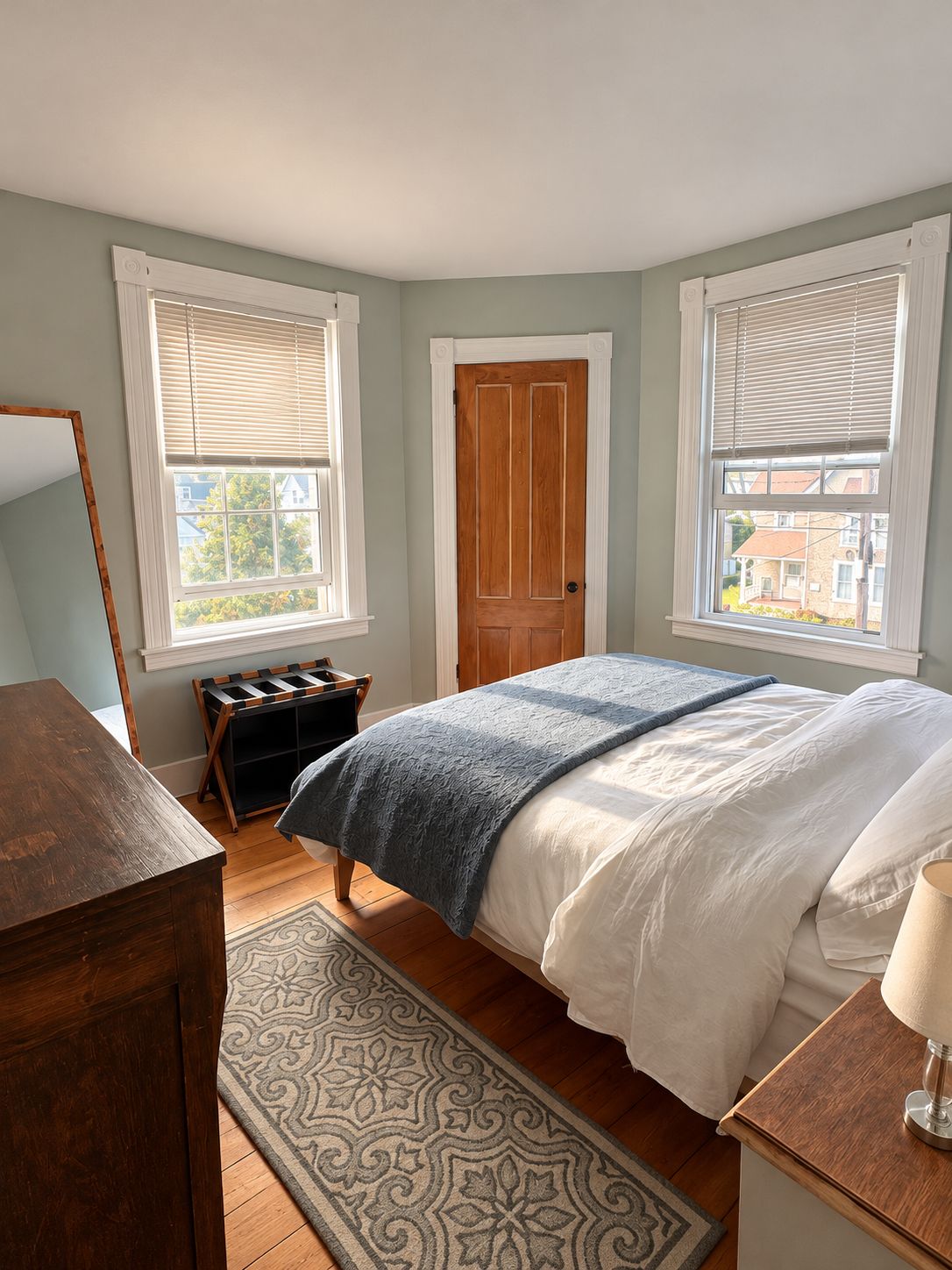 A bedroom with a bed, a dresser, a nightstand, a window with blinds, and a door.