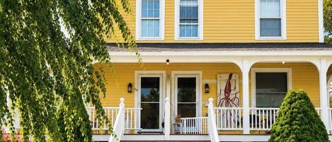 A two-story yellow house with a front porch, a staircase, and a well-maintained lawn.