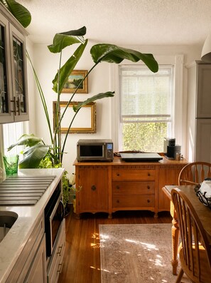 A kitchen with a wooden cabinet, a microwave, a coffee maker, and a dining table with chairs. - The Yellow House - Walk to Downtown Mystic (Stonington)