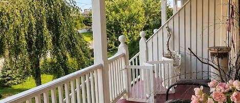 A covered porch with a railing, wicker furniture, and a table with flowers.