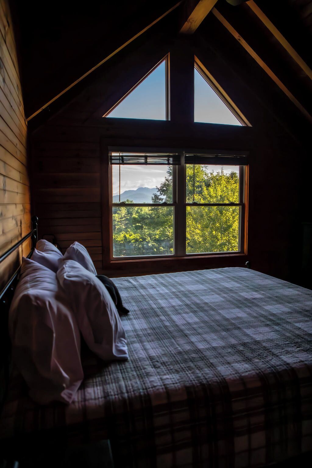Ein Schlafzimmer mit einem großen Fenster, einem Bett mit kariertem Überwurf und Holzwänden.