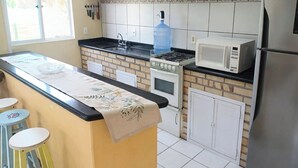 Uma cozinha com ilha central, armários brancos, geladeira, micro-ondas e bebedouro.