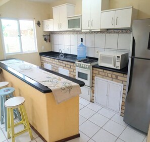 A kitchen with a central island, white cabinets, a refrigerator, a microwave, and a water dispenser. - 4-bedroom house 200 meters from Canto Grande beach, pets allowed. (Bombinhas)