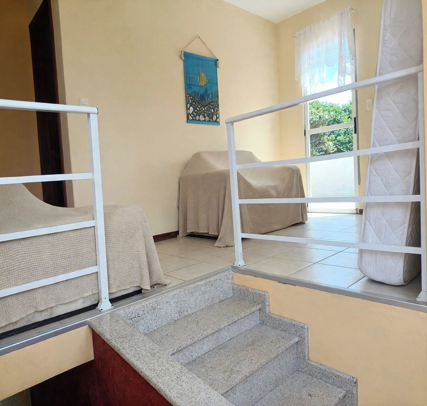 Una habitación de hotel con una cama, una mesita, una silla, una ventana con cortinas y una escalera.