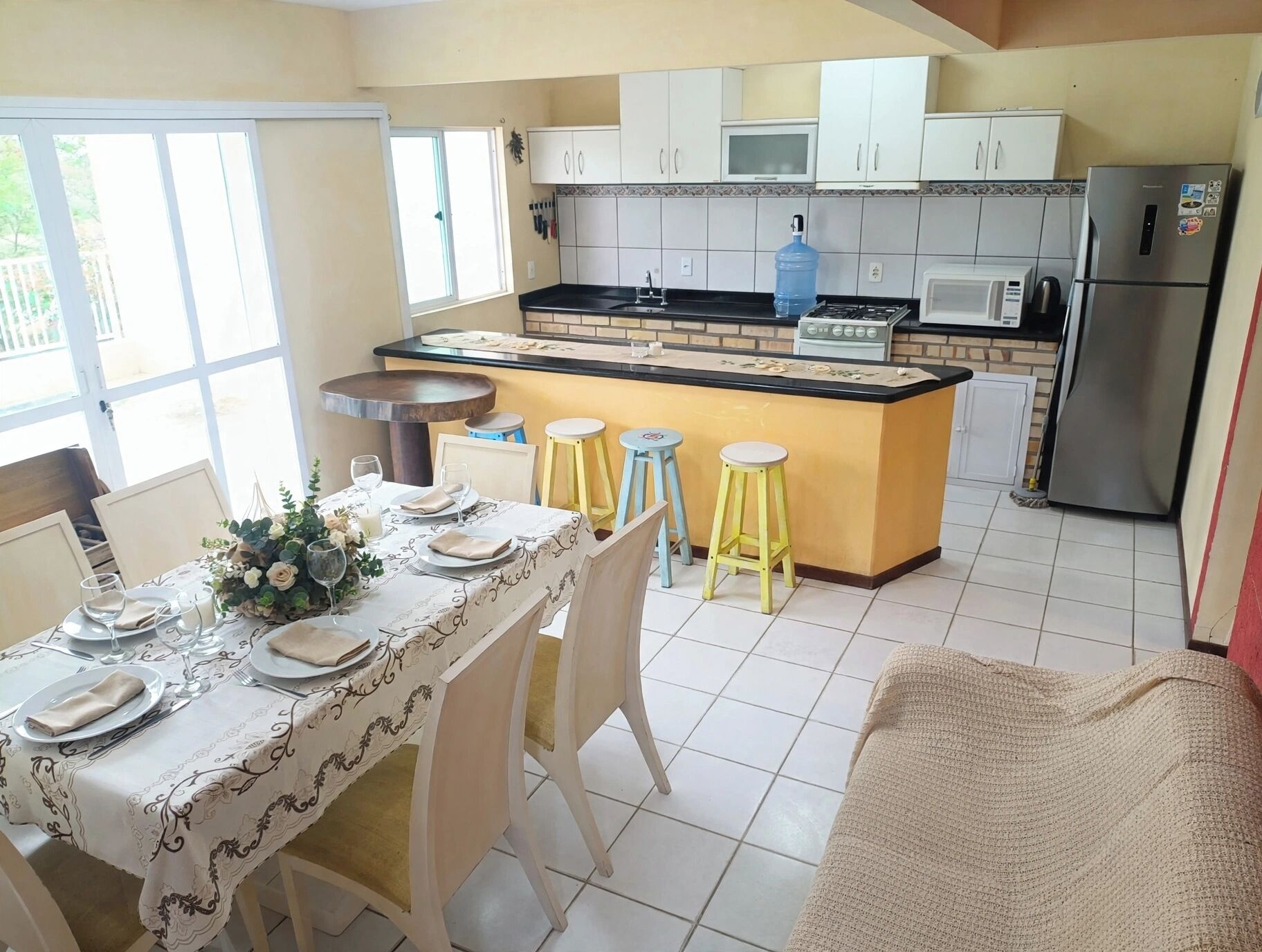 A kitchen with a central island, white cabinets, a refrigerator, and a dining area with a table set for four.