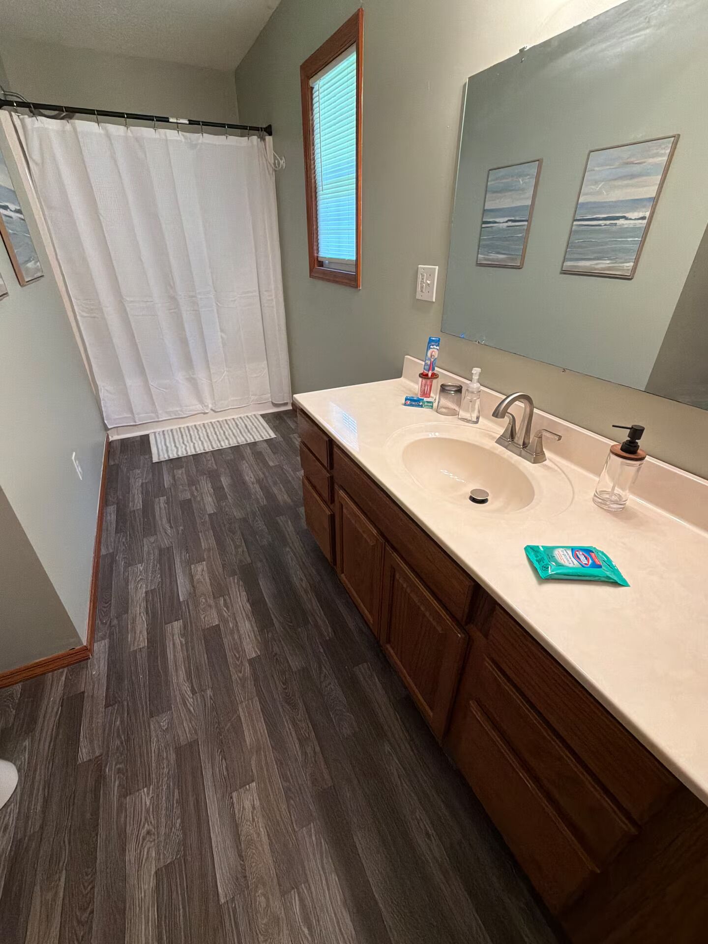 Un bagno con tenda doccia, lavandino con specchio e mobiletti in legno.