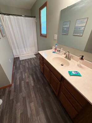 A bathroom with a shower curtain, a sink with a mirror, and wooden cabinets.